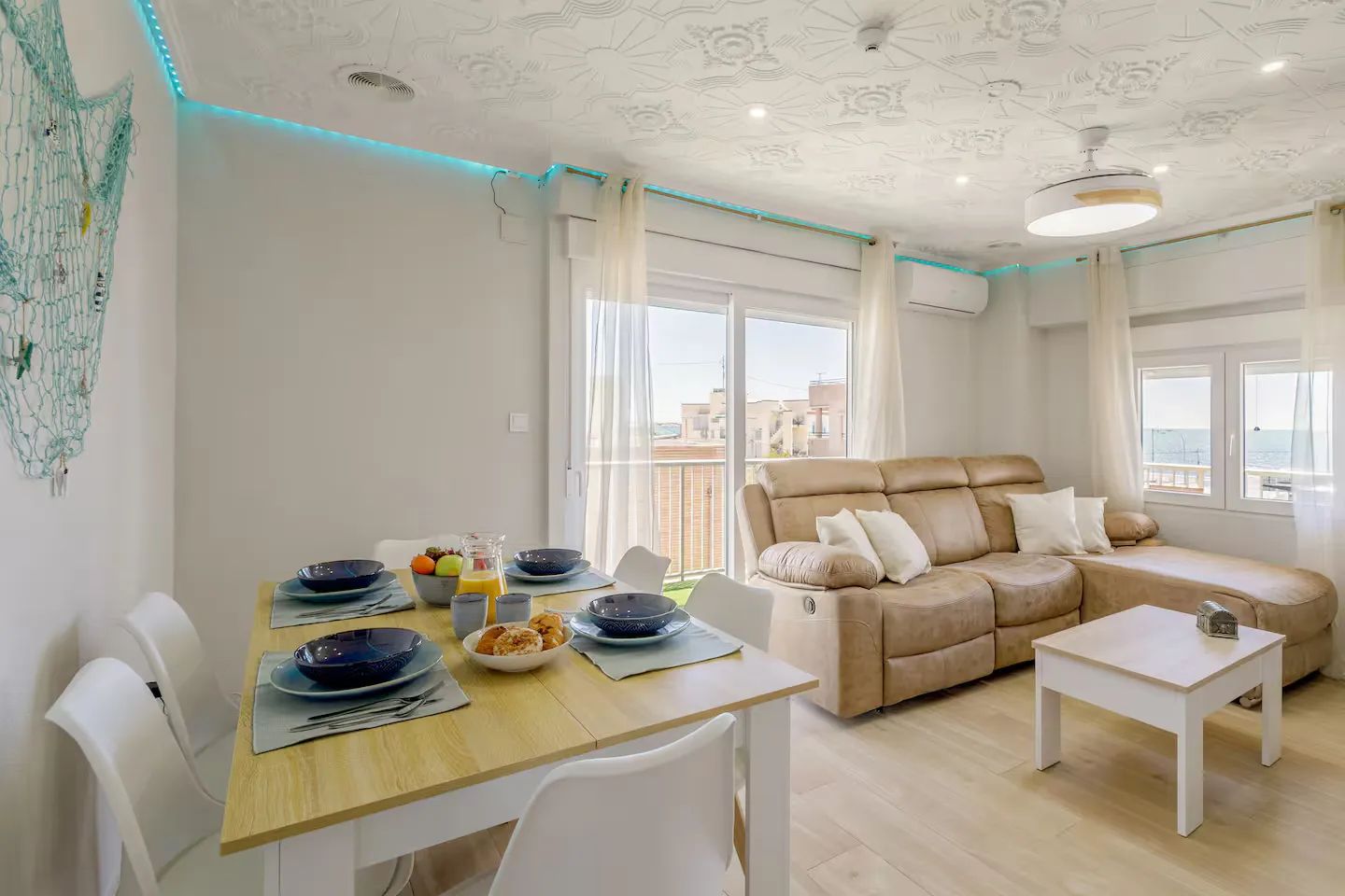Salón comedor luminoso con mesa puesta y vistas al mar, en un apartamento turístico de Santa Pola