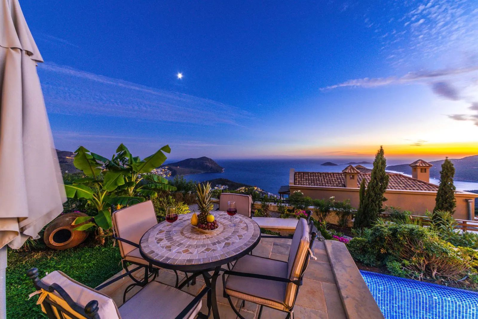 Terrace with a mosaic table and chairs, garden and pool, with sea views at dusk